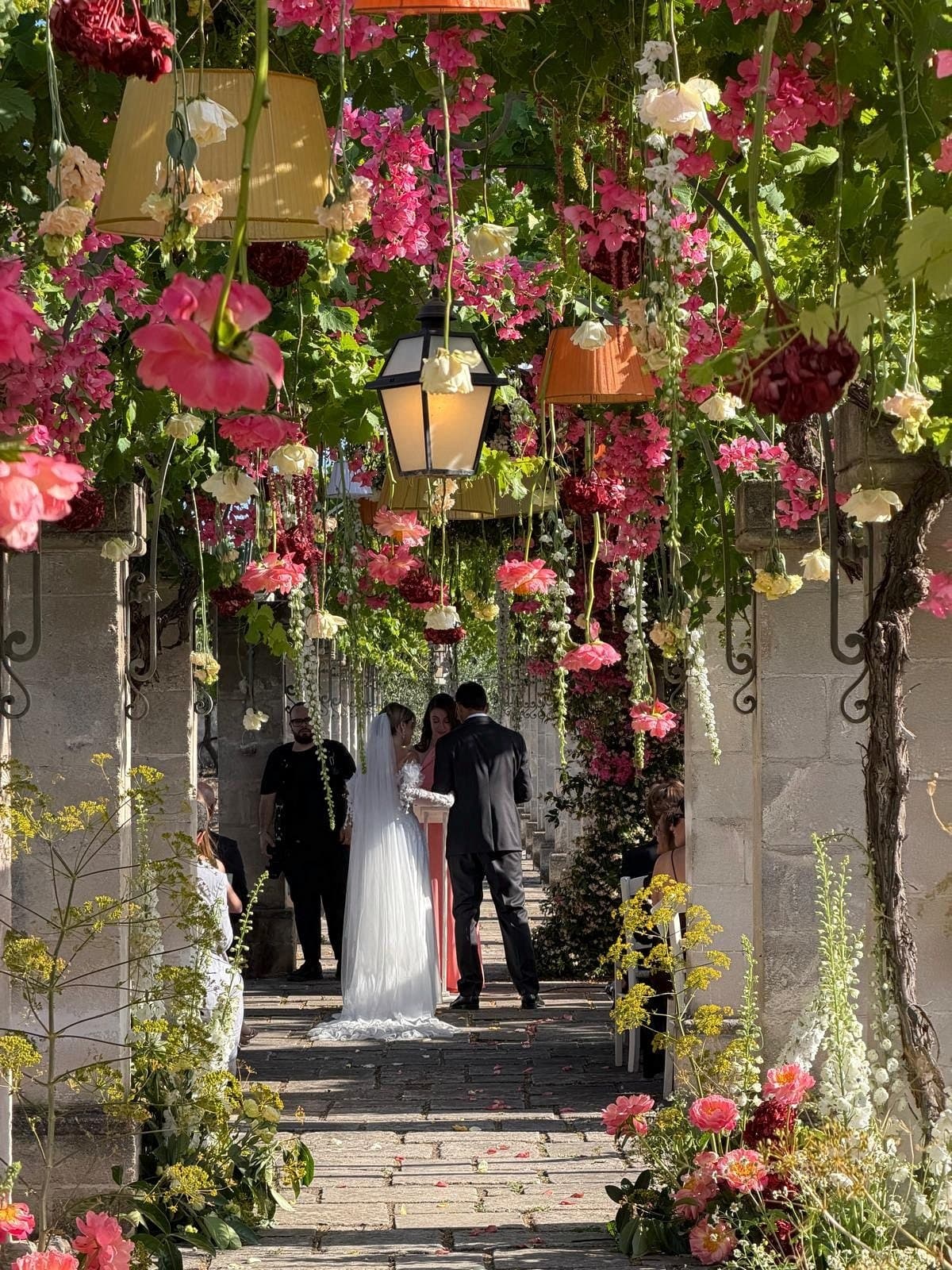 The couple with the celebrant under the pergola of flowers and lanterns